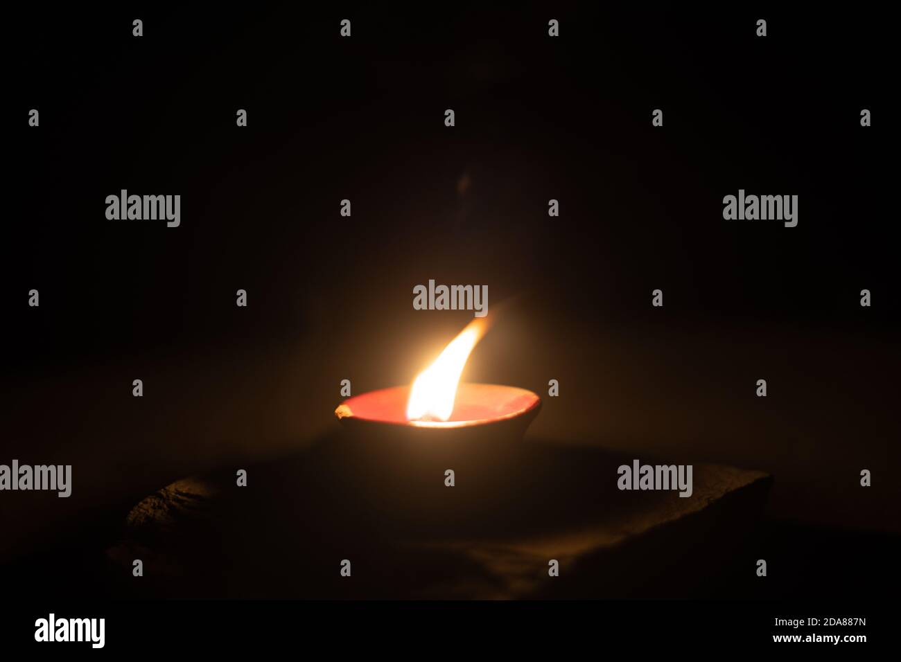Dunkles minimalistisches Bild, das eine Diya-Öllampe mit Öl oder Ghee gefüllt zeigt und einen Baumwolldocht verbrennt, um eine Flamme zu erzeugen, ist ein beliebtes religiöses Objekt und Stockfoto