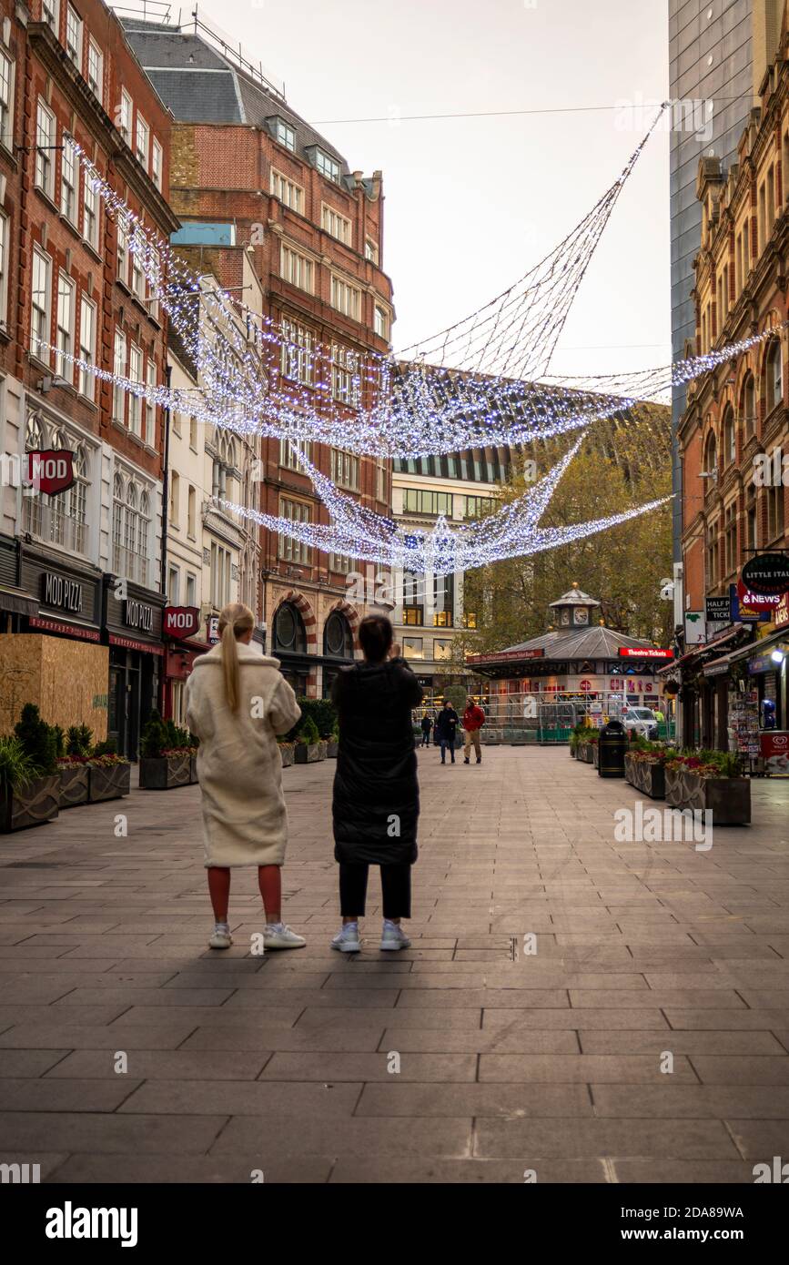 Zwei Frauen, die die Weihnachtsbeleuchtung im Leicester Square betrachten, während der COVID 19-Sperre leer. Geschlossene Restaurants. Schließen Sie Gastgewerbe-Unternehmen Stockfoto