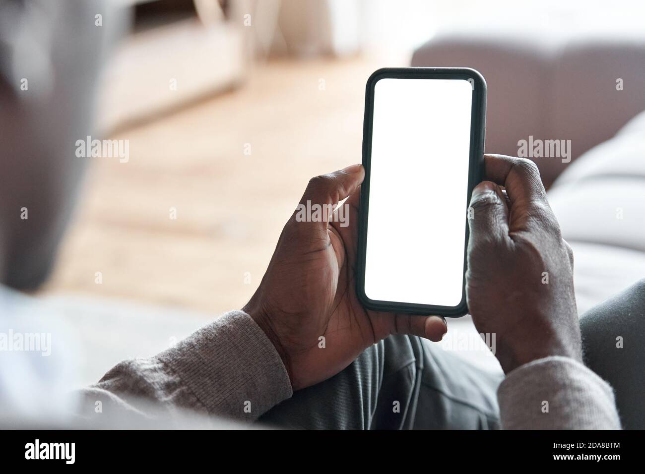 Afrikanischer Mann hält Telefon mit Mockup weißen Bildschirm für App-Anzeigen zu Hause. Stockfoto