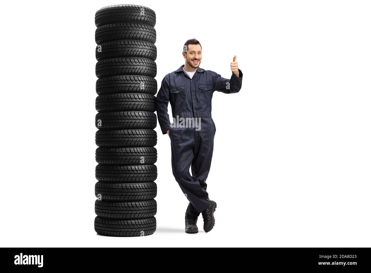 In voller Länge Porträt eines Auto-Mechaniker Arbeiter lehnt sich an Ein Haufen Autoreifen und zeigt Daumen nach oben isoliert Auf weißem Hintergrund Stockfoto