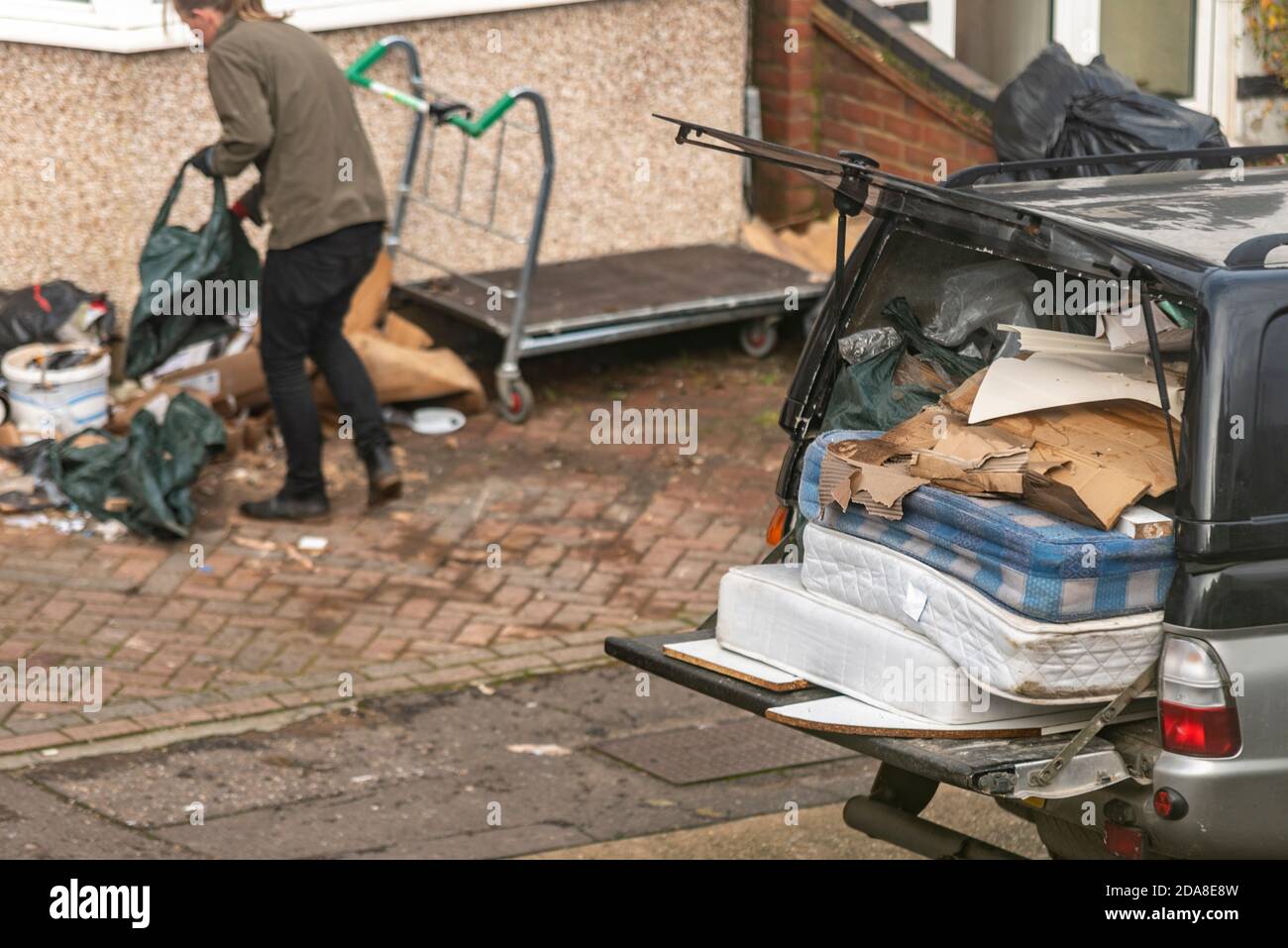 Eine Person, die Müll in den hinteren Teil eines Pick-up-Trucks lädt, einschließlich alter Matratzen. Abfallentsorgung in ungewöhnliche, kleine Fahrzeuge für den Aufgabenbereich Stockfoto