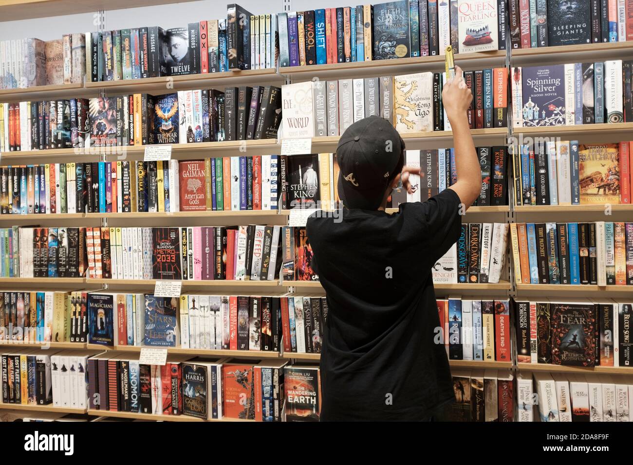 Teenage Boy, Alter 13-14, müde Gace Maske Auswahl Bücher in Buchhandlung, London, UK Stockfoto