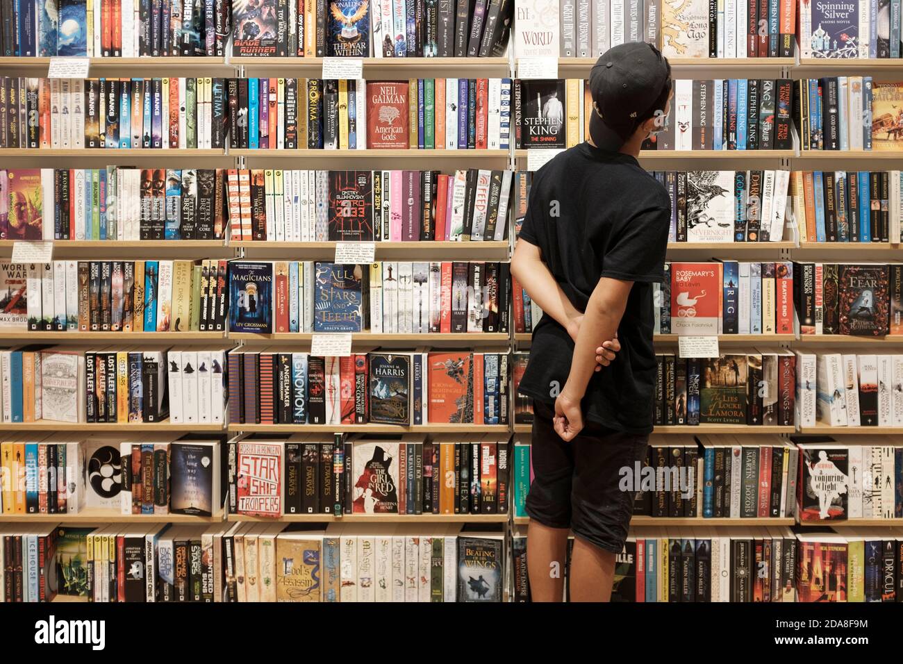 Teenage Boy, 13-14, trägt Gesichtsmaske wählt Bücher im Buchladen, London, Großbritannien Stockfoto
