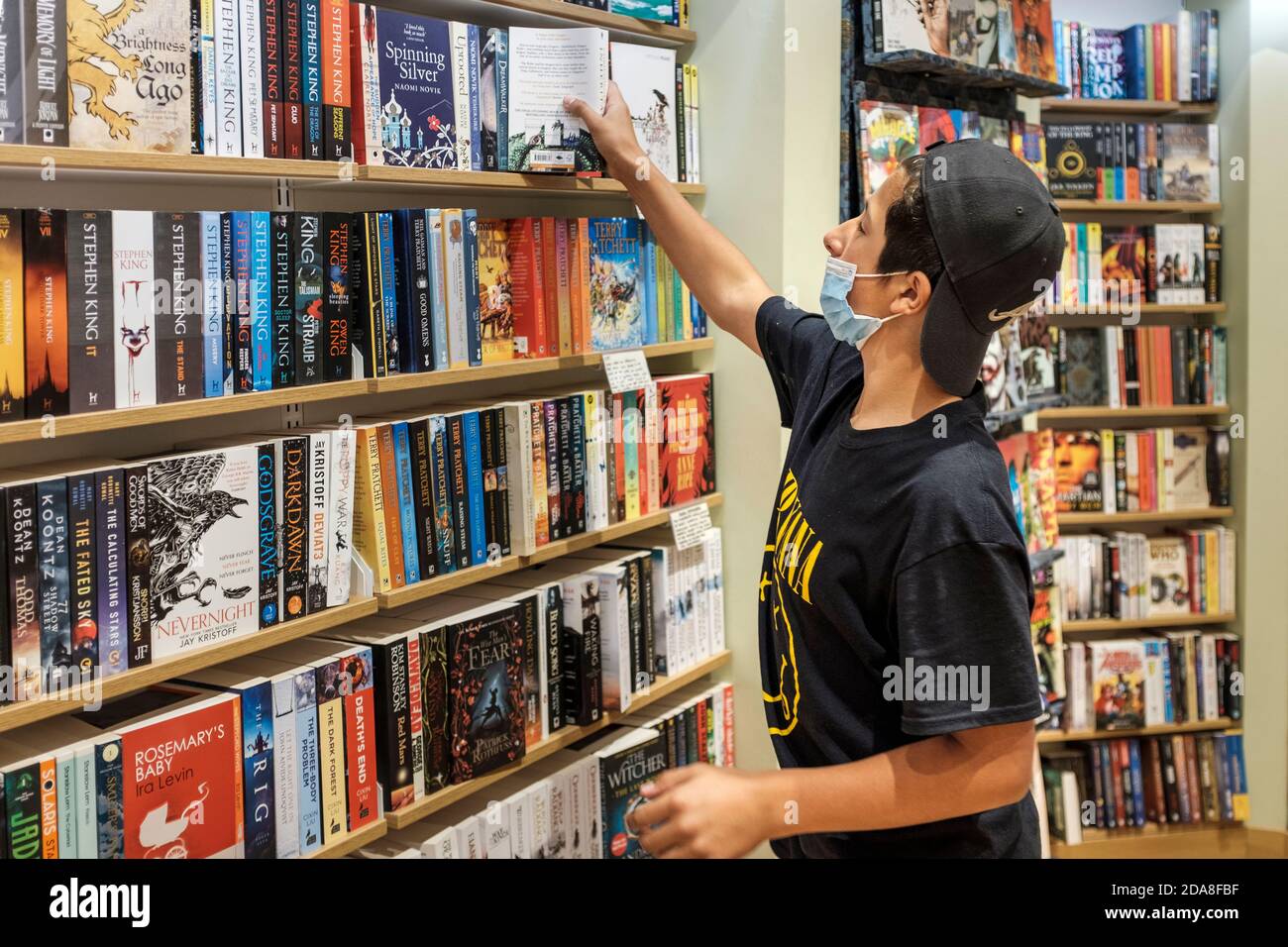 Teenage Boy, Alter 13-14, müde Gace Maske Auswahl Bücher in Buchhandlung, London, UK Stockfoto