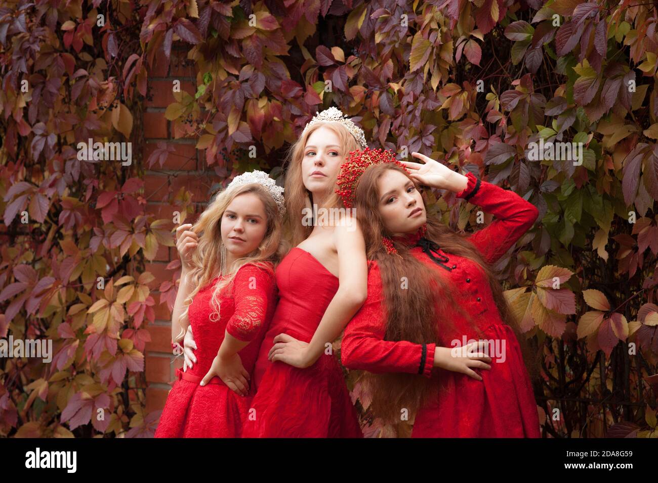 Russische Mädchen sind schön. Russische nationale Traditionen. Schwestern in Kronen. Ehefrauen aus dem Ausland. Freundinnen in roten Kleidern Stockfoto