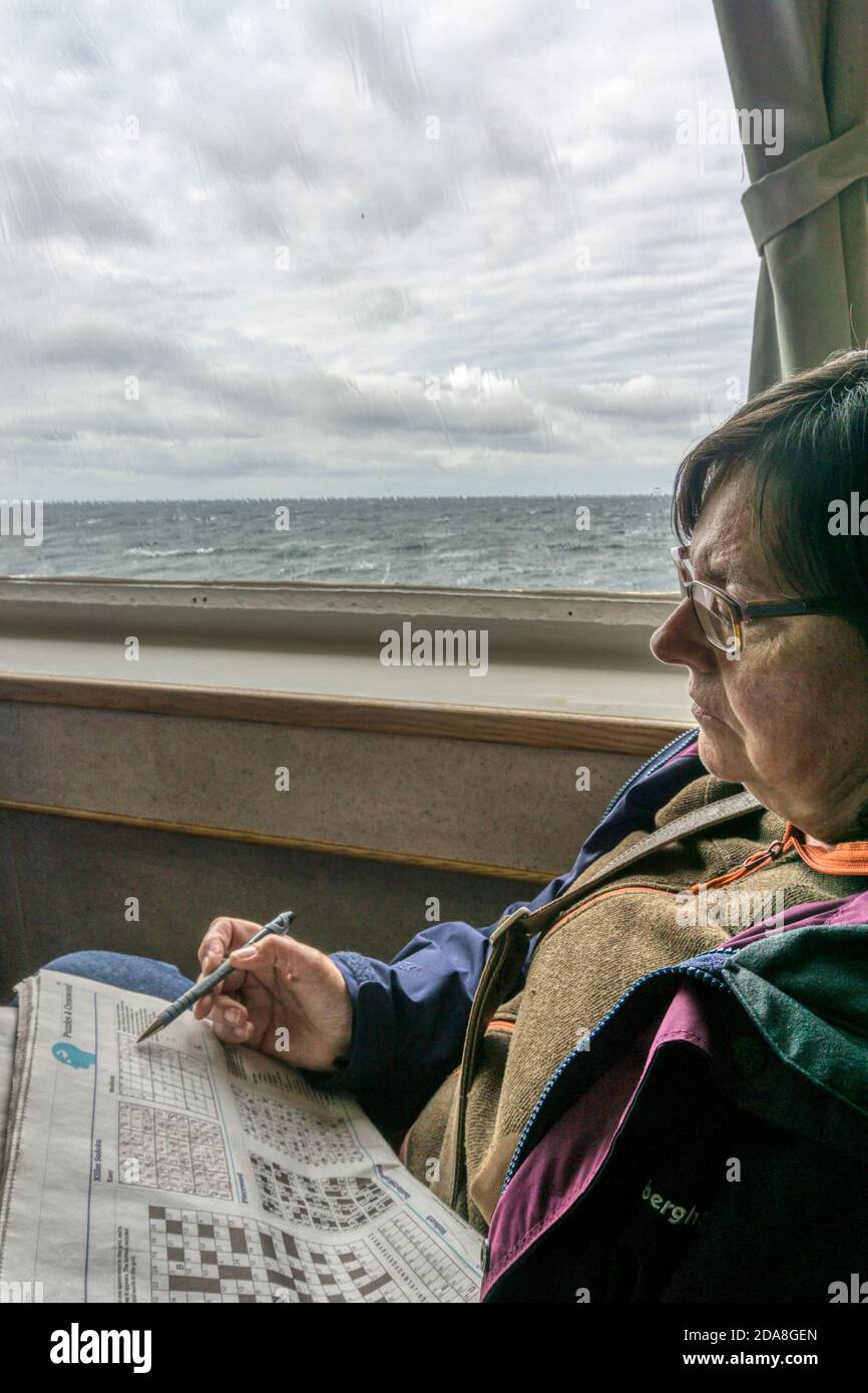 Frau, die ein Kreuzworträtsel macht, um die Zeit auf einer Fährreise zu den Äußeren Hebriden zu verstreichen. Stockfoto