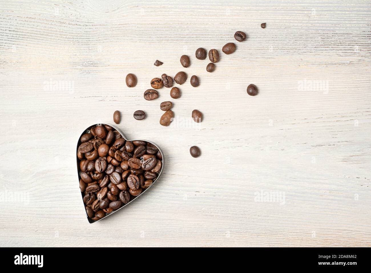 Herz aus Kaffeebohnen in Form eines fliegenden Kometen auf hellem Hintergrund. Draufsicht mit Platz zum Kopieren. Stockfoto