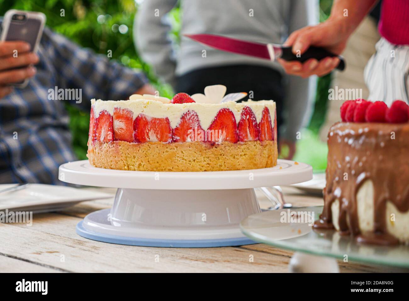 Hausgemachte Erdbeerkuchen auf dem Tisch im Freien mit unkenntlichen Menschen im Hintergrund. Geringe Schärfentiefe. Stockfoto