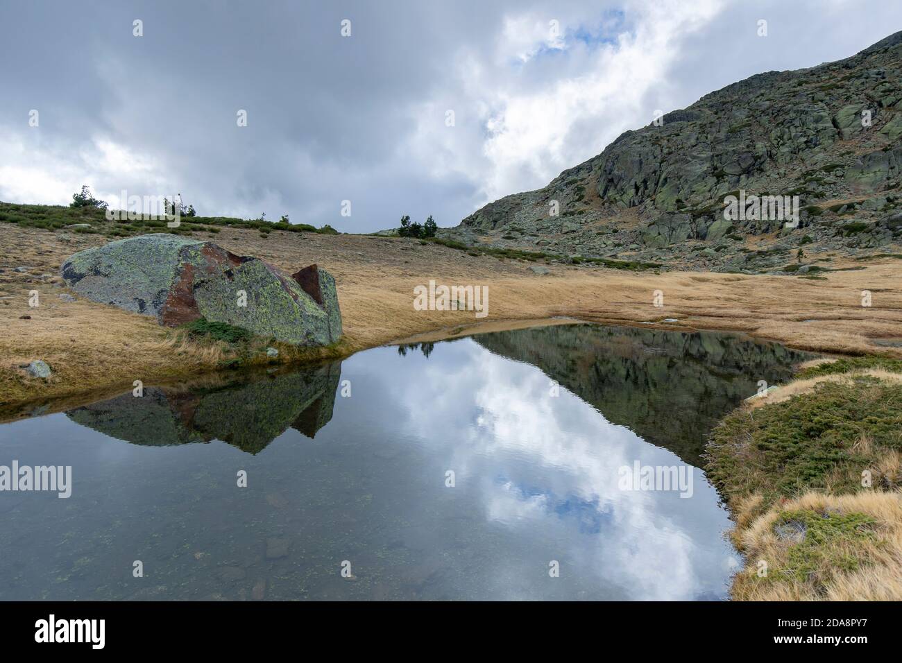 Hochgebirge tarn, der die Granitgipfel von Peñalara an einem ruhigen Sommermorgen im Nationalpark Sierra de Guadarrama in Zentralspanien reflektiert. Stockfoto