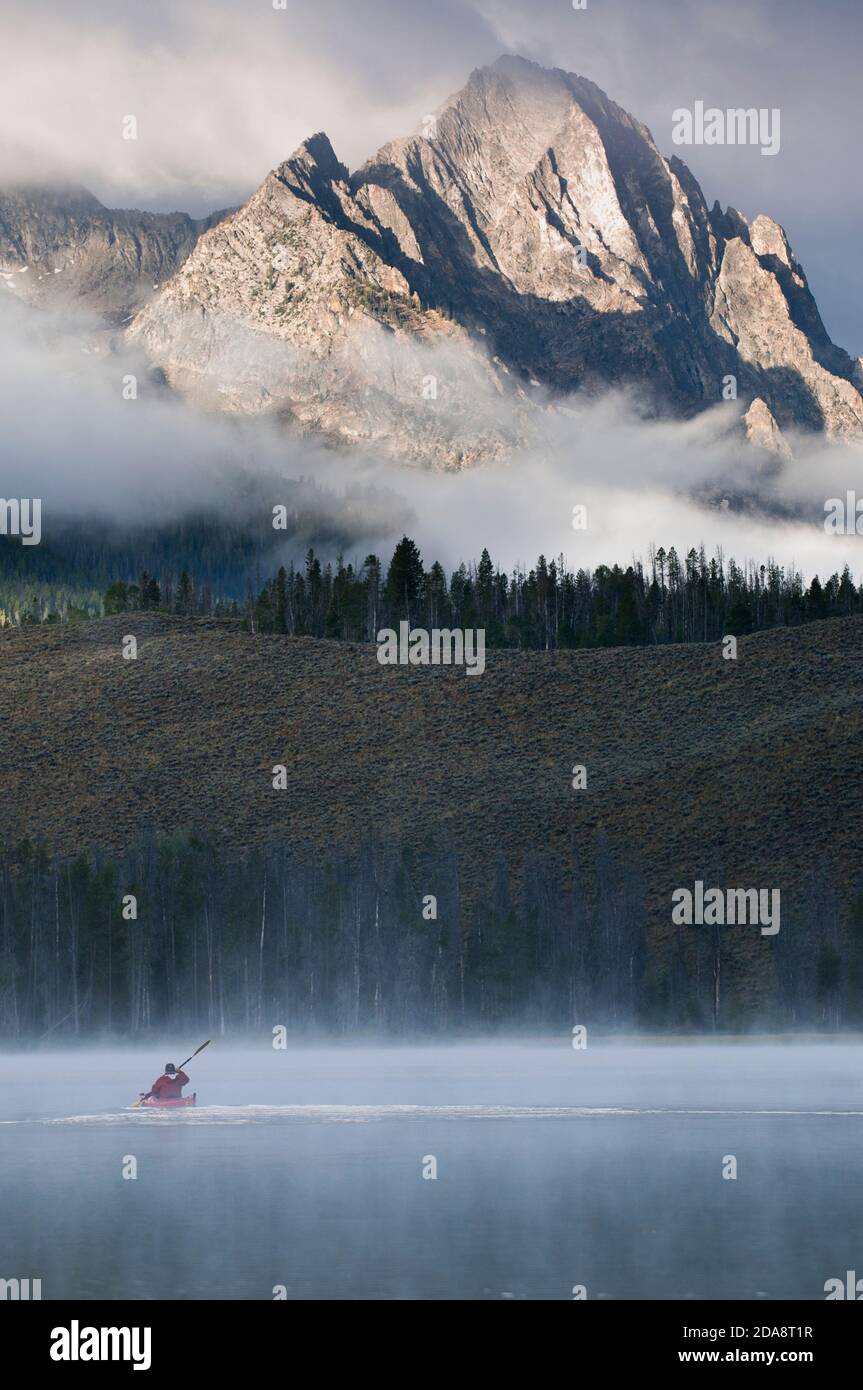 Ein Kajakfahrer paddelt durch den Nebel auf Little Redfish Lake unterhalb der Sawtooth Mountains in Stanley, Idaho. Stockfoto