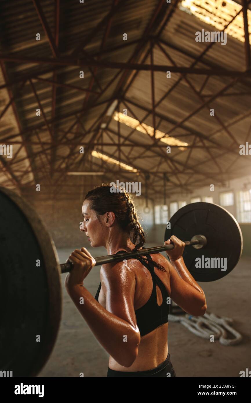 Fit Frau Training mit Langhantel mit schweren Gewichten in einem Fitnessstudio im leeren Lager. Weibliche tun Kniebeugen Übung. Stockfoto