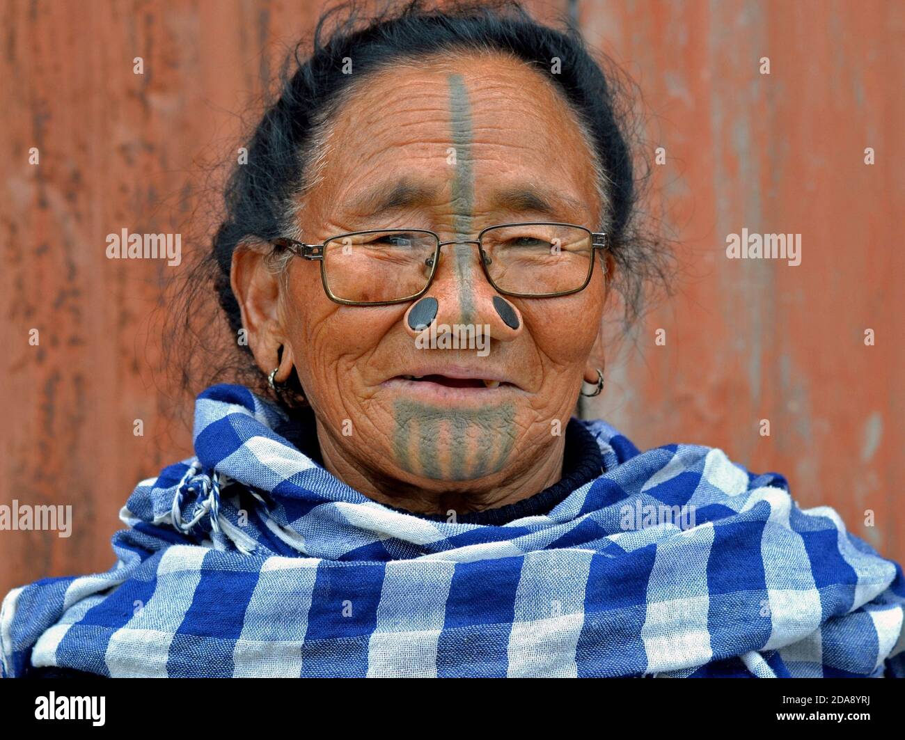 Alte nordöstliche indische Apatani Stammesfrau mit schwarzen hölzernen Nasenstopfen und traditionellem Gesichts-Tattoo trägt moderne Brillen und Posen für die Kamera. Stockfoto