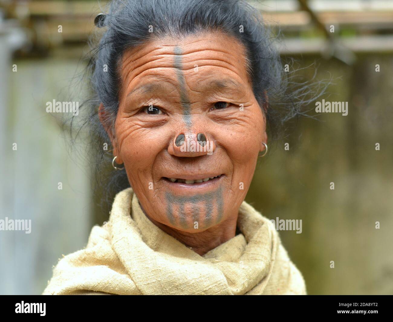 Ältere nordöstliche indische Apatani ethnische Minderheit Stammesfrau mit schwarzen hölzernen Nasenstopfen und traditionellen Gesichts-Tattoos lächelt für die Kamera. Stockfoto