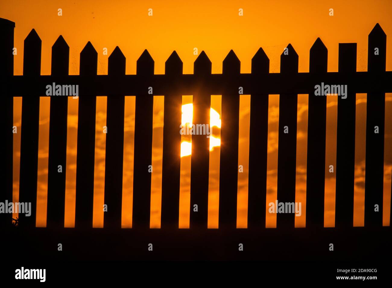 Sonnenuntergang und ein Zaun. Generisches Foto der Sonneneingangsaufnahme durch einen Pfostenzaun. Stockfoto