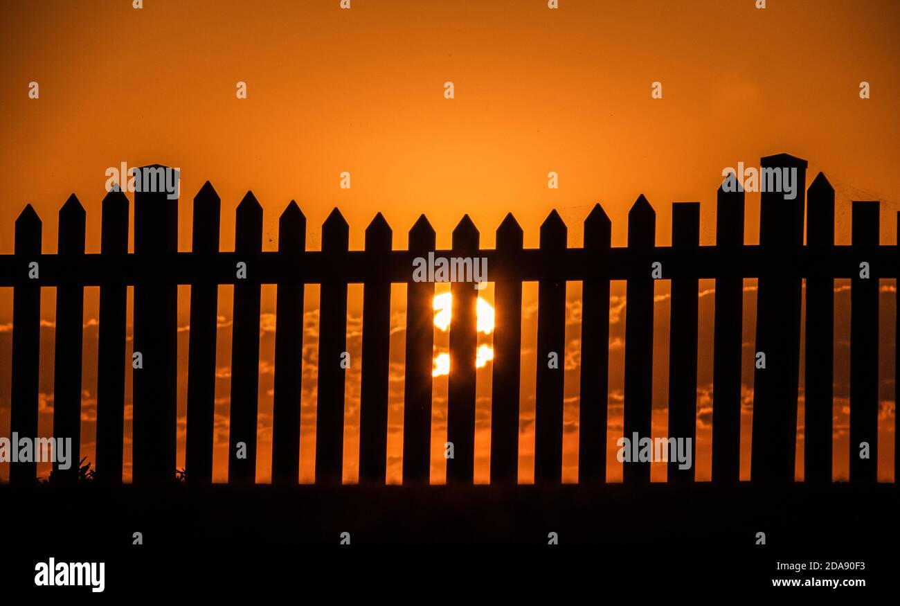 Sonnenuntergang und ein Zaun. Generisches Foto der Sonneneingangsaufnahme durch einen Pfostenzaun. Stockfoto