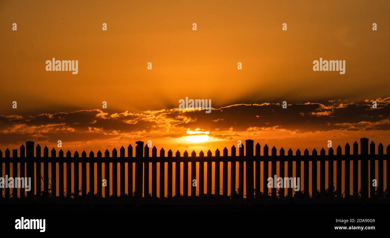 Sonnenuntergang und ein Zaun. Generisches Foto der Sonneneingangsaufnahme durch einen Pfostenzaun. Stockfoto