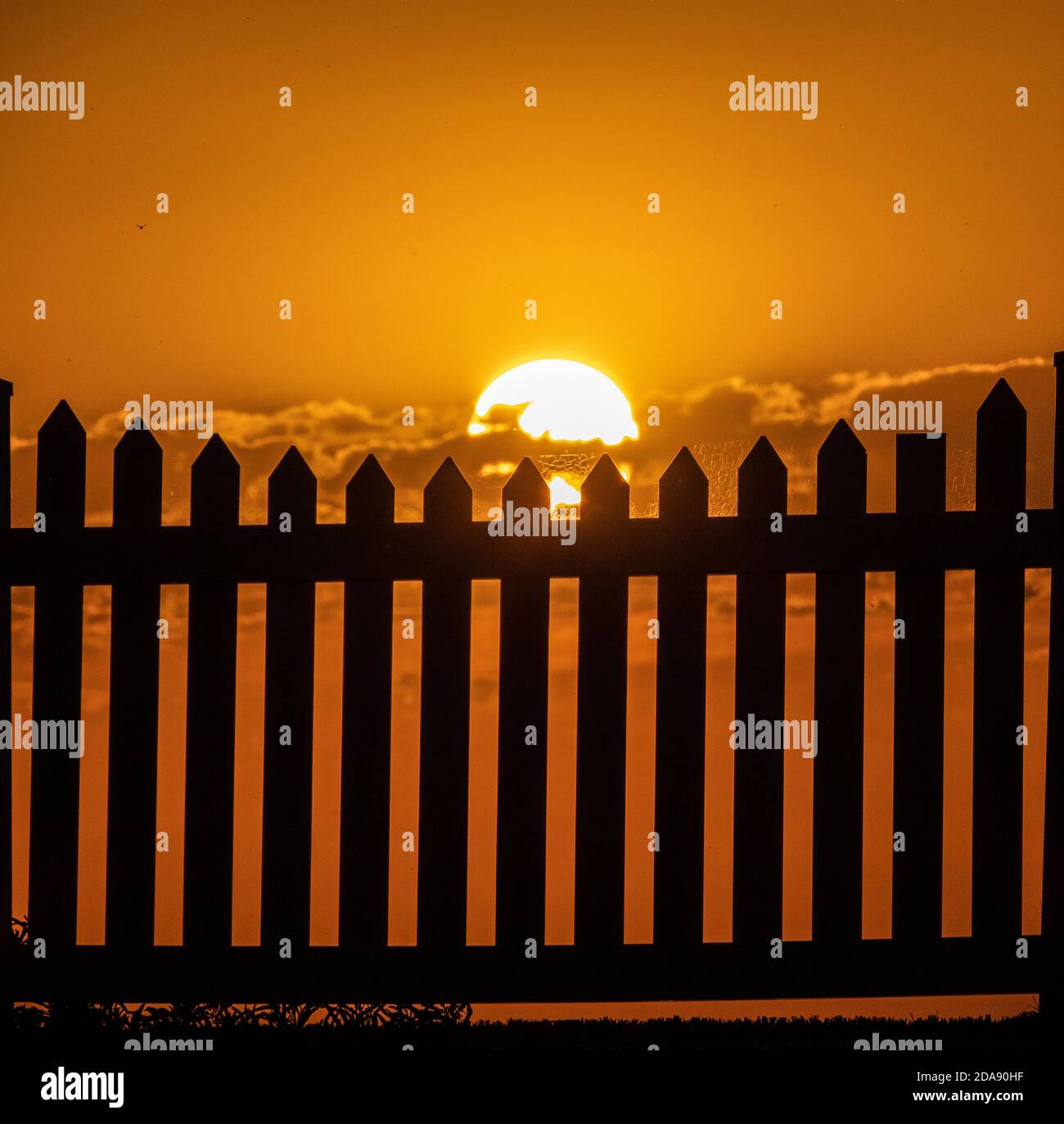 Sonnenuntergang und ein Zaun. Generisches Foto der Sonneneingangsaufnahme durch einen Pfostenzaun. Stockfoto