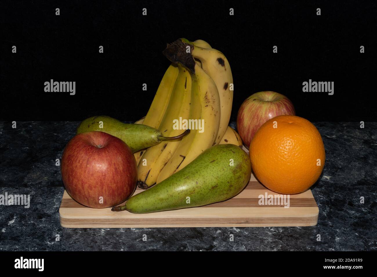 Primer plano de imagen de frutas, plátanos, manzanas peras y naranja colocadas sobre mesa y fondo oscuro Stockfoto