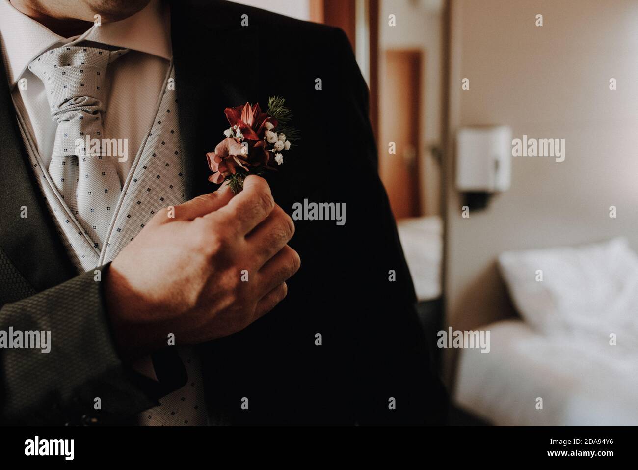Ein Bräutigam legt eine Blumennadel auf das Revers seiner Jacke, Filmkorn hinzugefügt. Stockfoto
