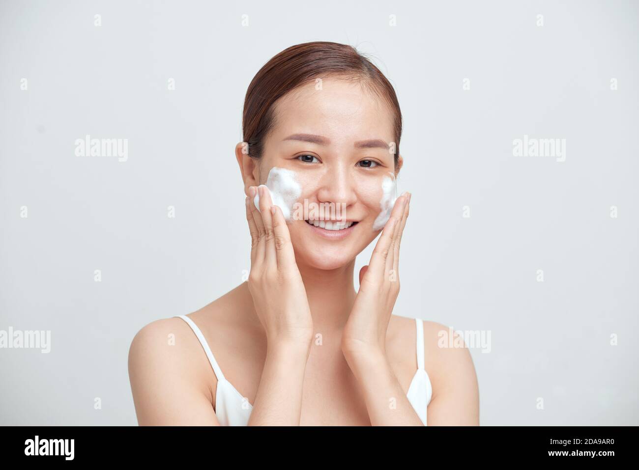 Fröhliche asiatische Frau Anwendung schäumende Reinigungsmittel, hat saubere frische gesunde Haut. Stockfoto