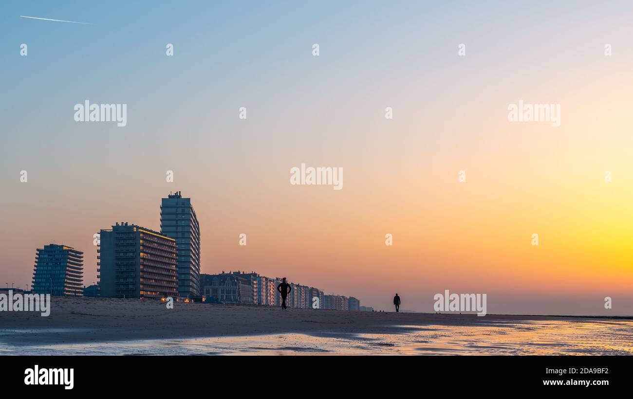 Silhouette von zwei Personen, die am Strand von Oostende (Ostende) bei Sonnenuntergang mit seiner Skyline an der Nordsee, Belgien, spazieren gehen. Stockfoto