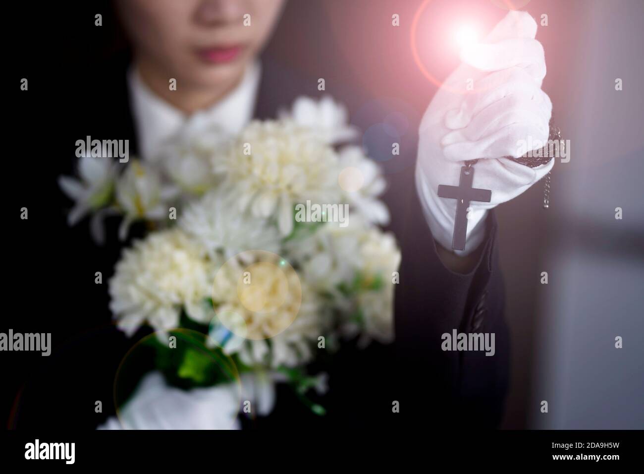 Hinterbliebene halten Kreuz mit Blumen bei der Beerdigung Stockfoto