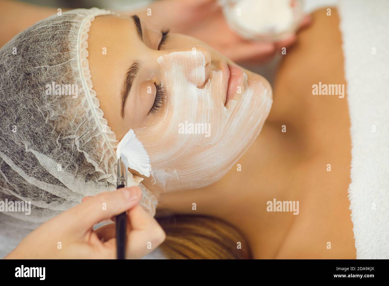 Kosmetologe deckt junge Frauen Gesicht mit feuchtigkeitsspendenden Maske mit Pinsel Stockfoto