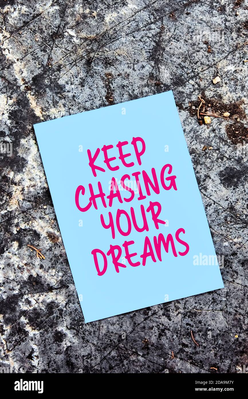 Halten Sie jagen Ihre Träume Zitat auf blauem Papier auf einem Felsen in der Natur geschrieben. Verfolgen Sie Ihr Traumkonzept. Stockfoto