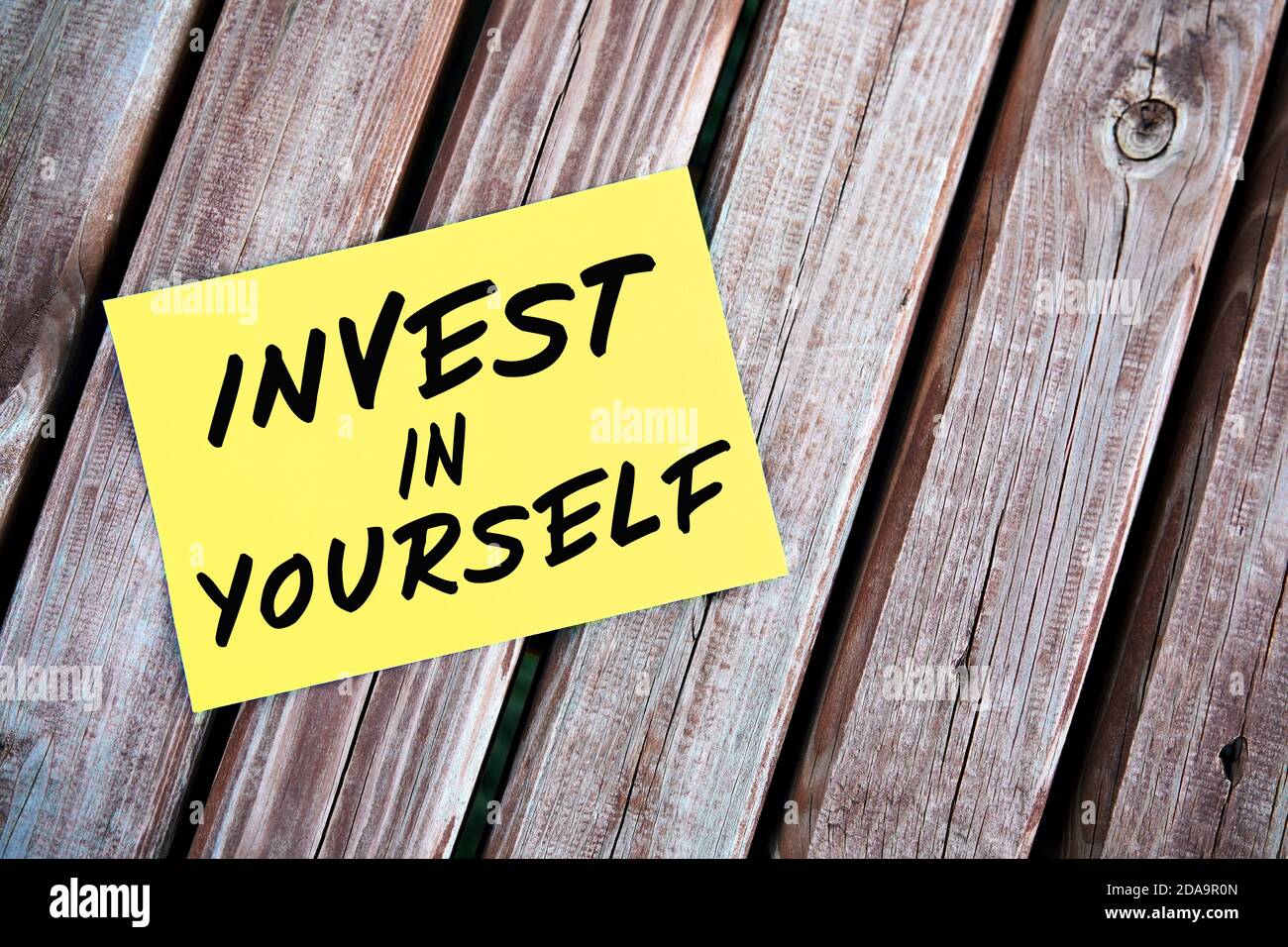 Investieren Sie in sich selbst Motivationszitat handschriftlich auf Papier auf einem Holztisch. Selbst- oder persönliches Entwicklungskonzept. Stockfoto