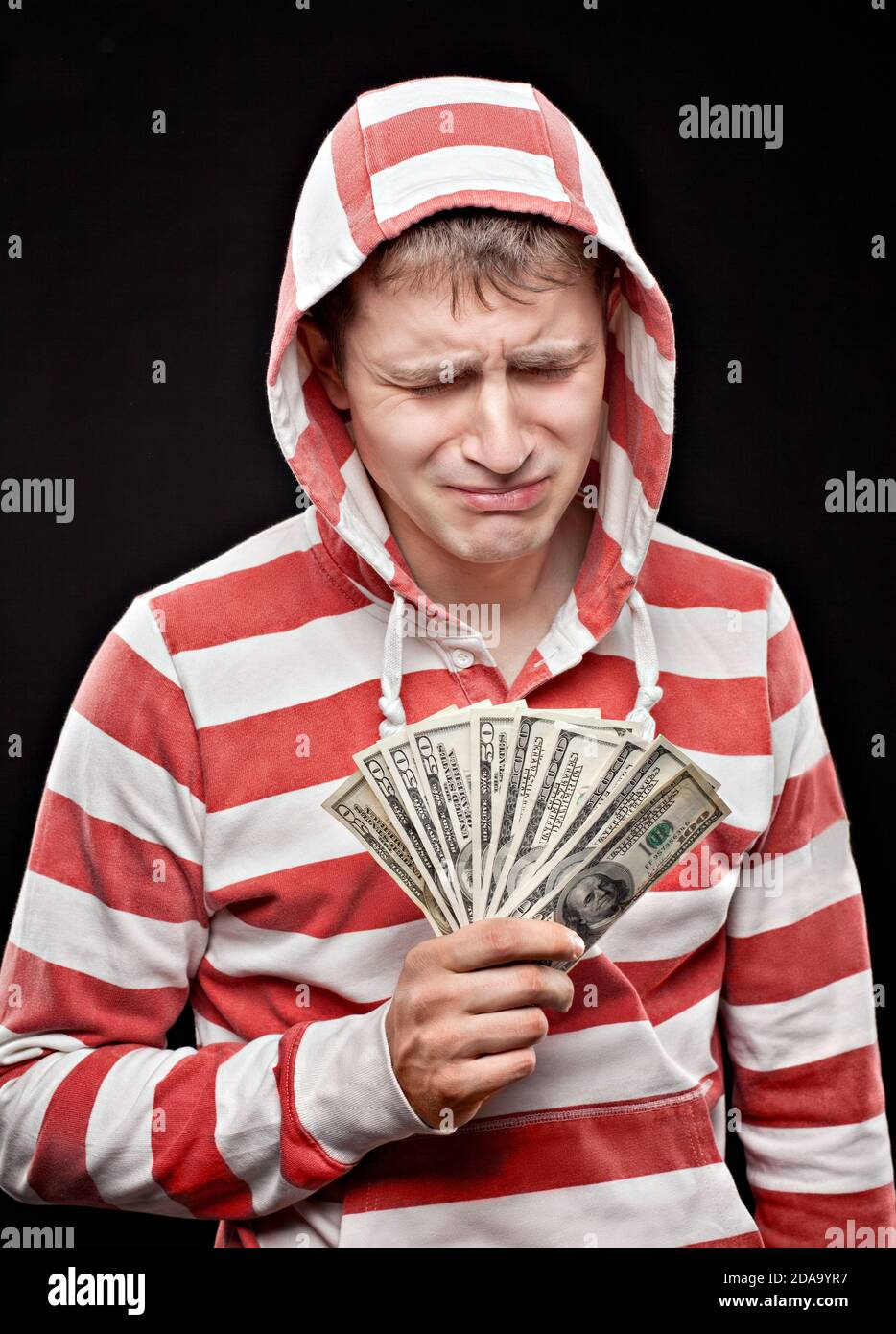 Weinender junger Mann mit Geldfan in den Händen Trägt eine Kapuze Stockfoto