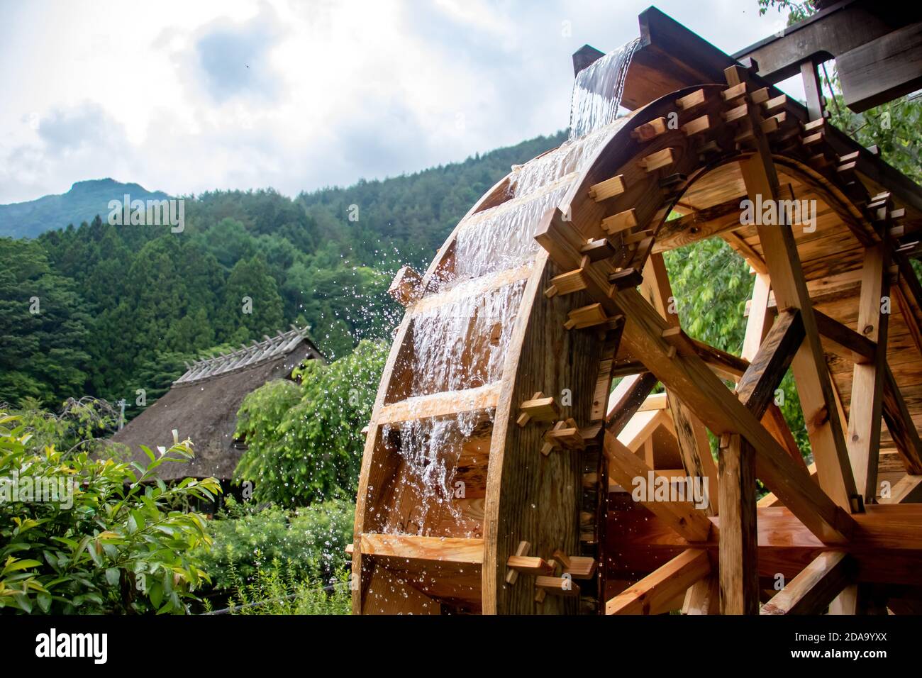 Das Mühlrad dreht sich unter einem Strom von Wasser, das Open Air Museum im Dorf mit traditionellen Reetdach Häusern Stockfoto