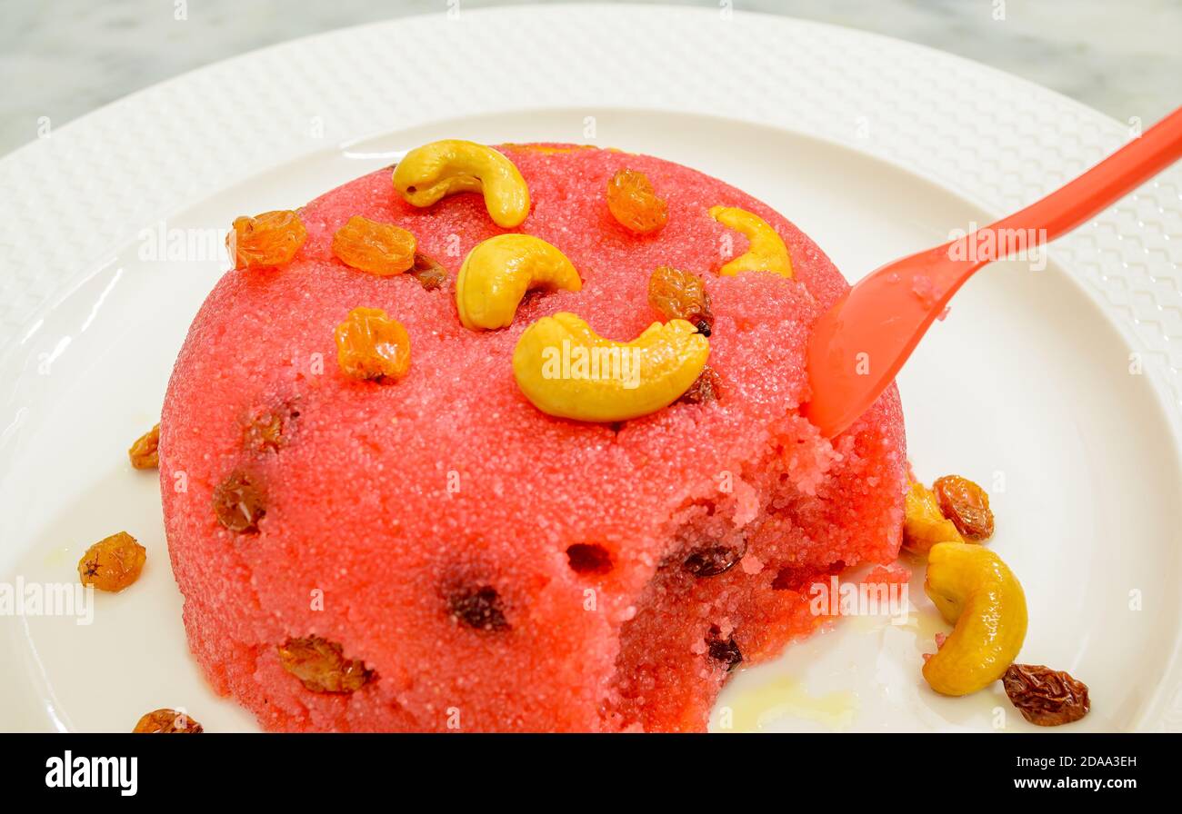 Pink Löffel getaucht in einem halb gefressenen Rava Kesari Gericht garniert Mit Cashewnüssen & Rosinen Stockfoto