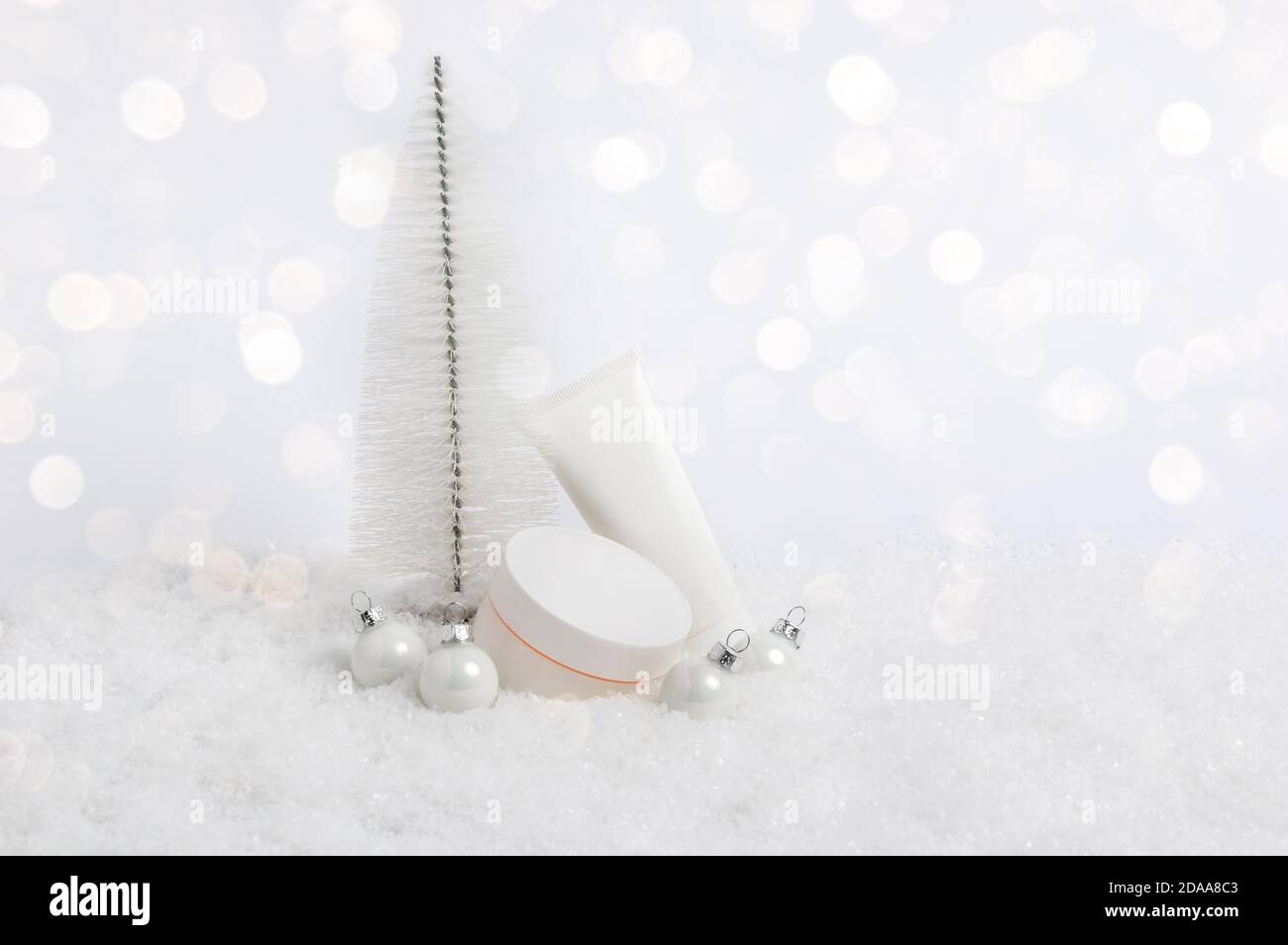Set von Winter Hautpflege Kosmetik-Produkte im Schnee mit Weihnachtsbaum und Kugeln in weißem Ton und Bokeh Lichter. Gesichts- und Handcreme Stockfoto