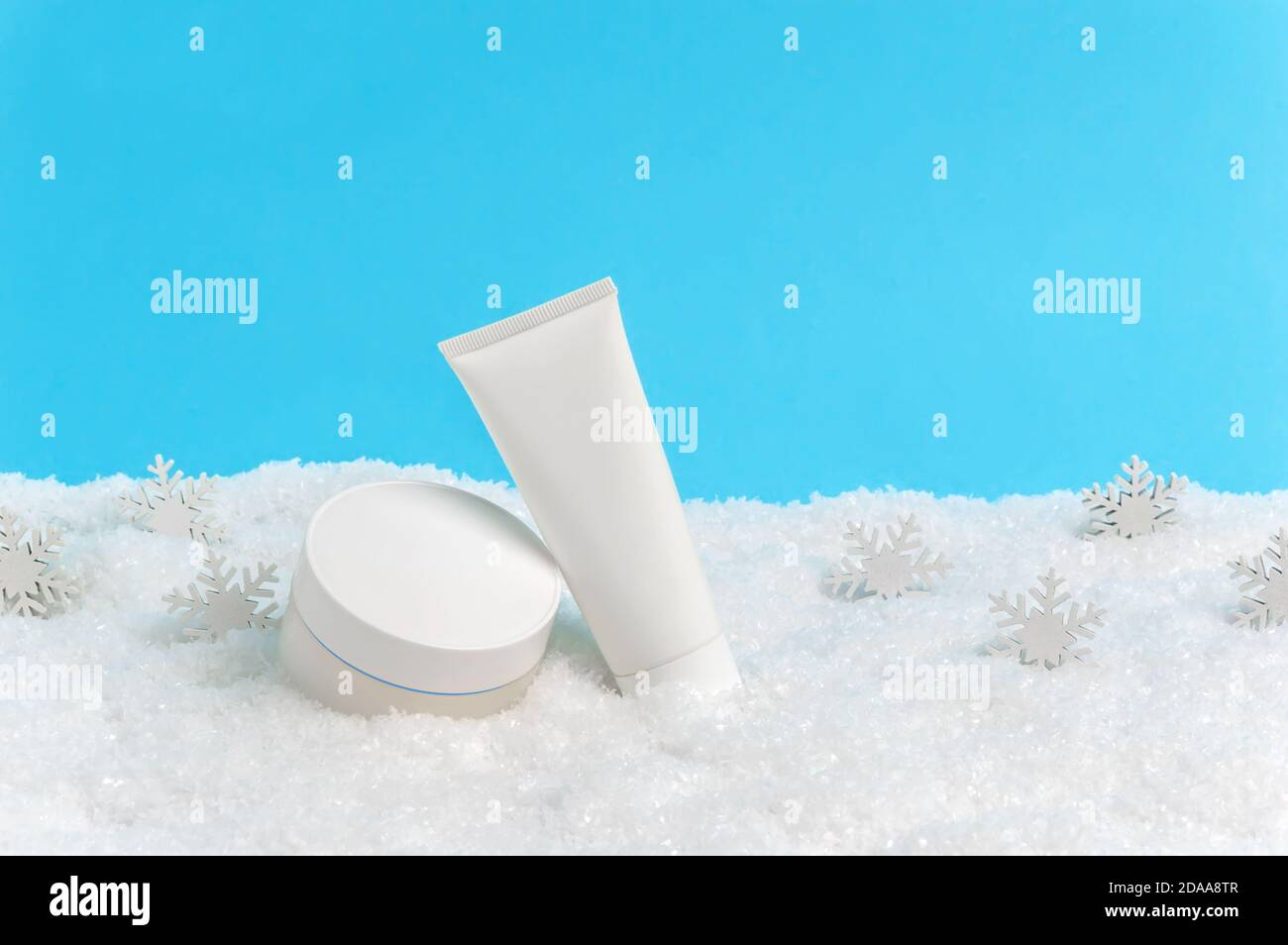 Gesichtscreme Glas und Handcreme oder Körperlotion Tube in Schnee und Schneeflocken auf blauem Hintergrund. Winter Hautpflege Kosmetik-Produkte. Saisonal kaltes Wetter Stockfoto