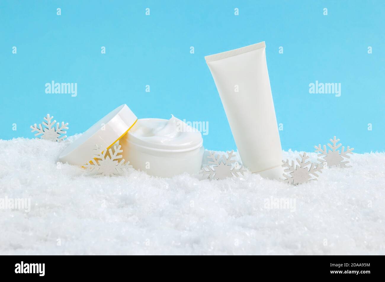 Geöffnetes Gesichts-Creme-Glas und Handcreme oder Körperlotion Tube im Schnee und Schneeflocken auf blauem Hintergrund. Winter Hautpflege Kosmetik-Produkte Stockfoto