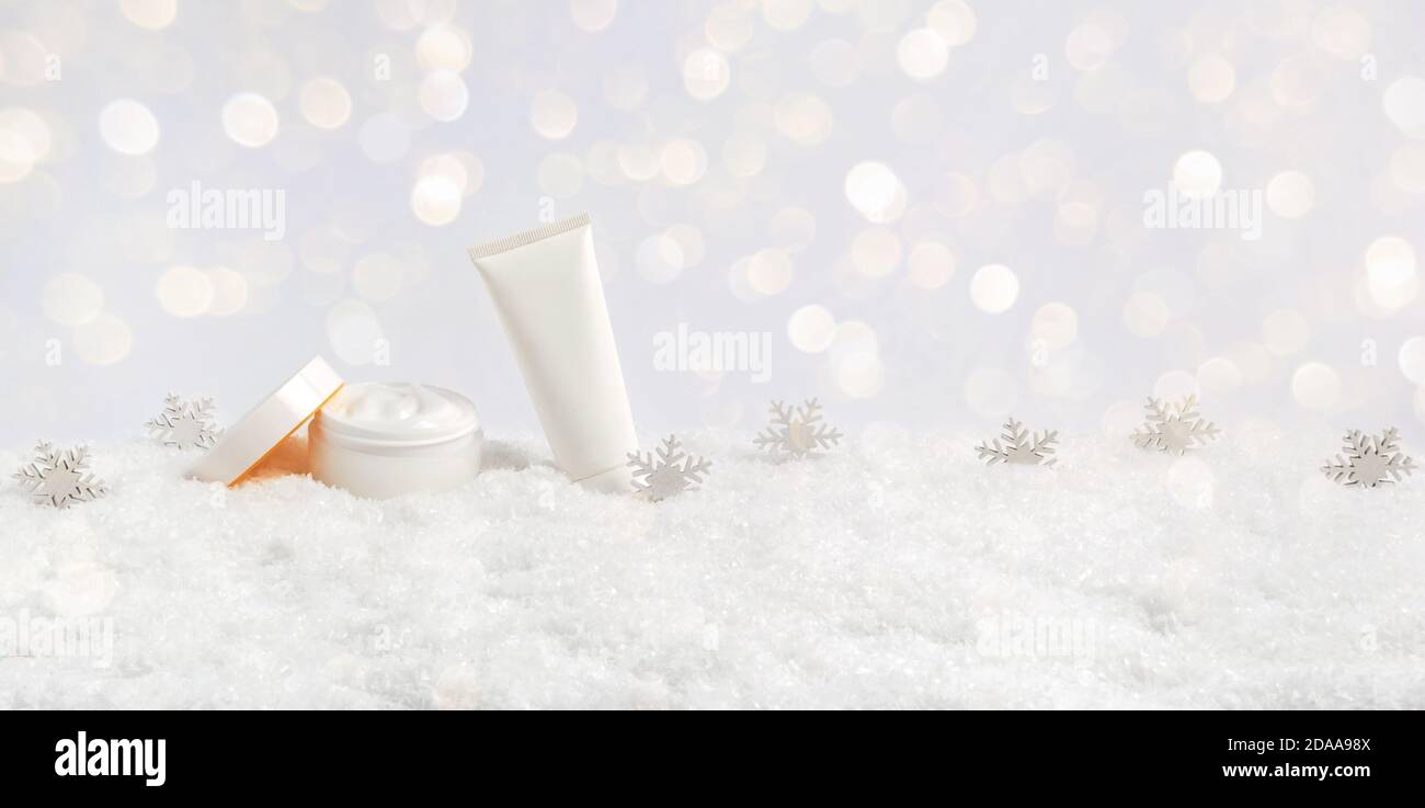 Winter Hautpflege Kosmetik-Produkte in Schnee und Schneeflocken auf weißem Hintergrund mit Bokeh Lichter. Offenes Gesichts-Cremeglas und Handcreme oder Körperlotion Stockfoto