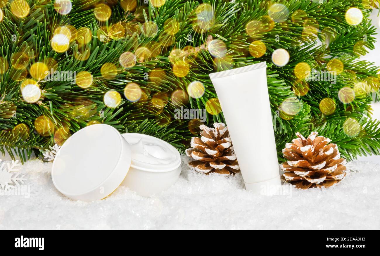 Set von Winter Hautpflege Kosmetik-Produkte im Schnee unter Weihnachtsbaum mit Pinienzapfen und Bokeh Lichter. Gesichtscreme und Handcreme oder Körperlotion Stockfoto