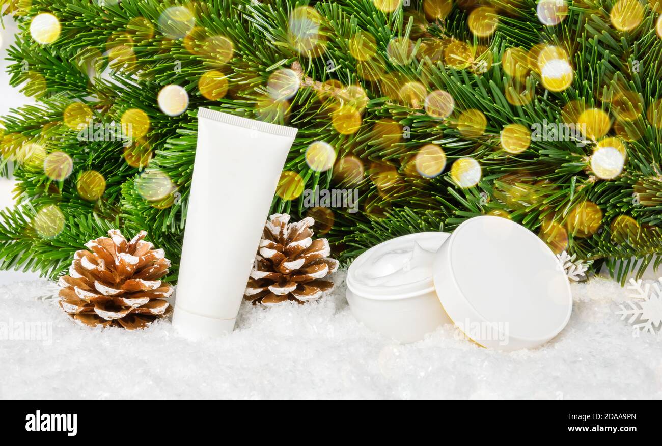 Winter Hautpflege Kosmetik-Produkte im Schnee unter Weihnachtsbaum mit Tannenzapfen und Bokeh Lichter. Gesichts-Creme-Glas und Handcreme oder Körperlotion Tube Stockfoto