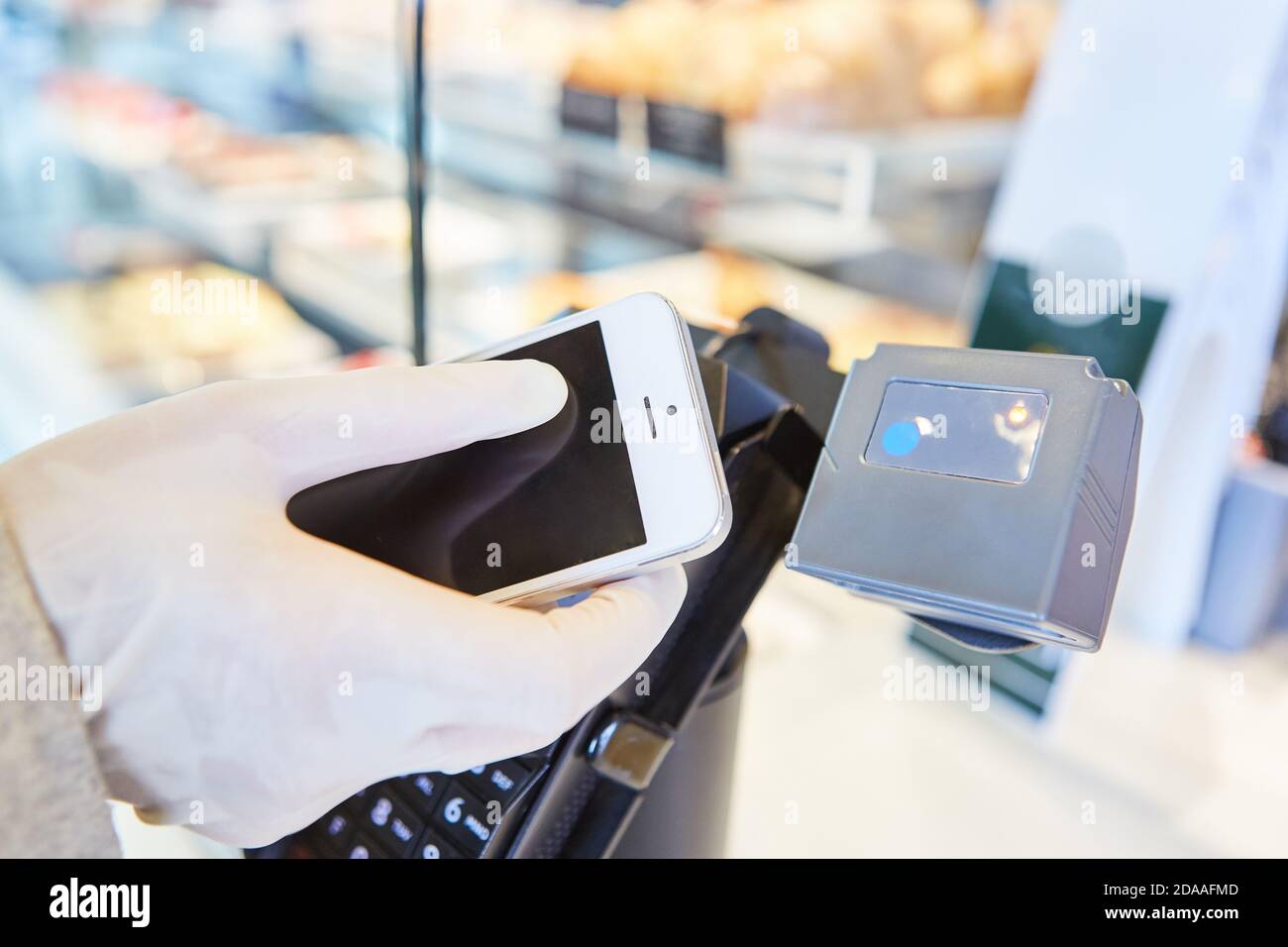 Hand in Einweghandschuhe mit Smartphone für mobile Zahlung bei Die Kasse Stockfoto