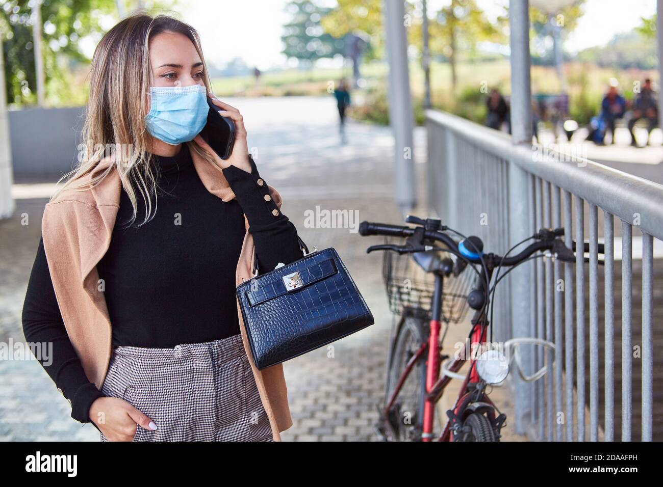 Junge Frau mit Gesichtsmaske wegen Covid-19 und Smartphone Im Stadtzentrum Stockfoto