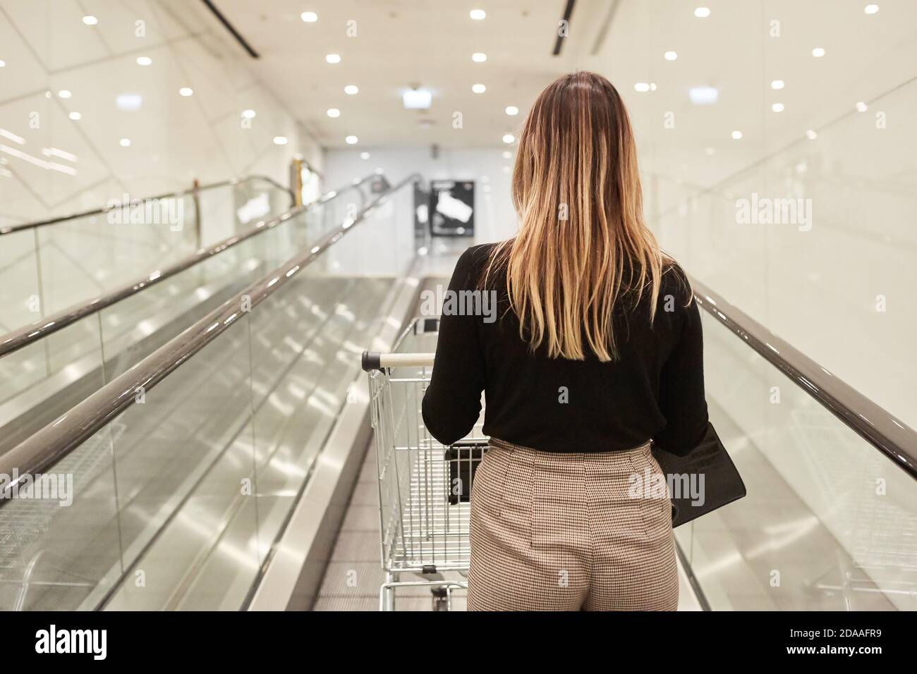 Frau als Kunde mit Einkaufswagen auf Rolltreppe in Einkaufszentrum Stockfoto