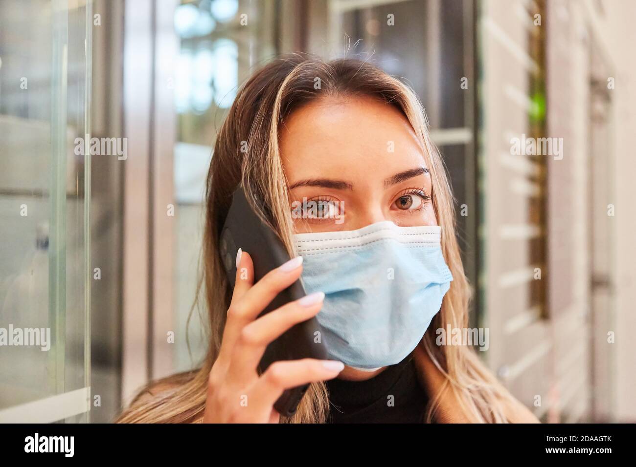 Frau mit Mund- und Nasenschutz wegen der Covid-19 Pandemie verwendet ein Mobiltelefon Stockfoto