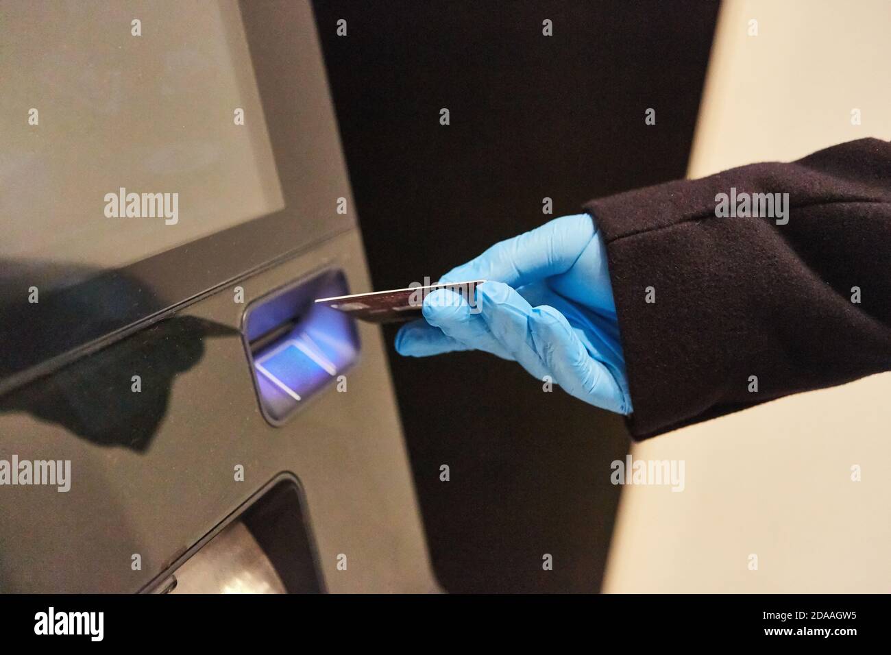 Hand in Einweghandschuhe legt Bankkarte in ATM während Covid-19 Pandemie Stockfoto