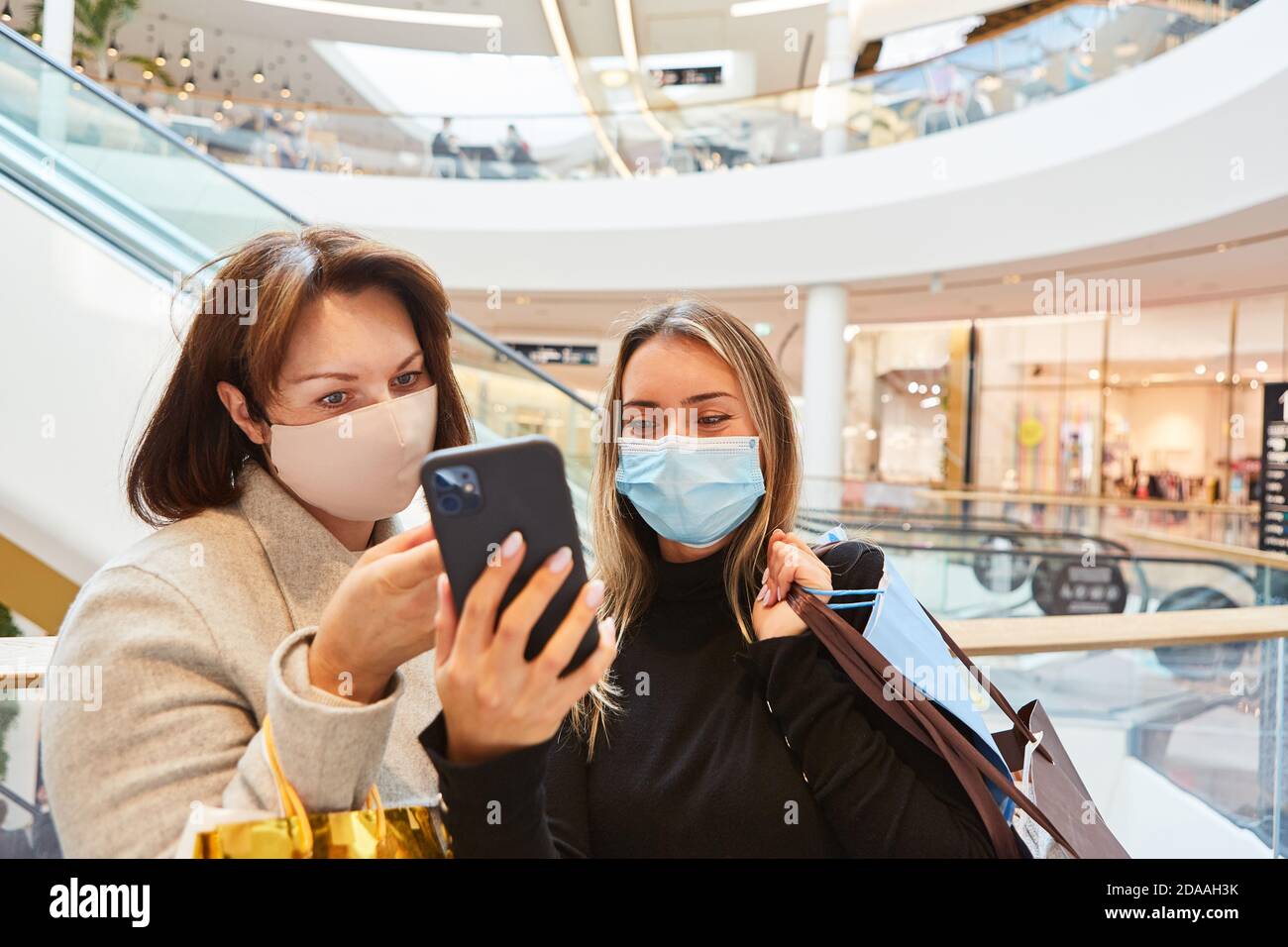 Frauen mit Gesichtsmasken wegen Covid-19 lesen SMS weiter Smartphone im Einkaufszentrum Stockfoto
