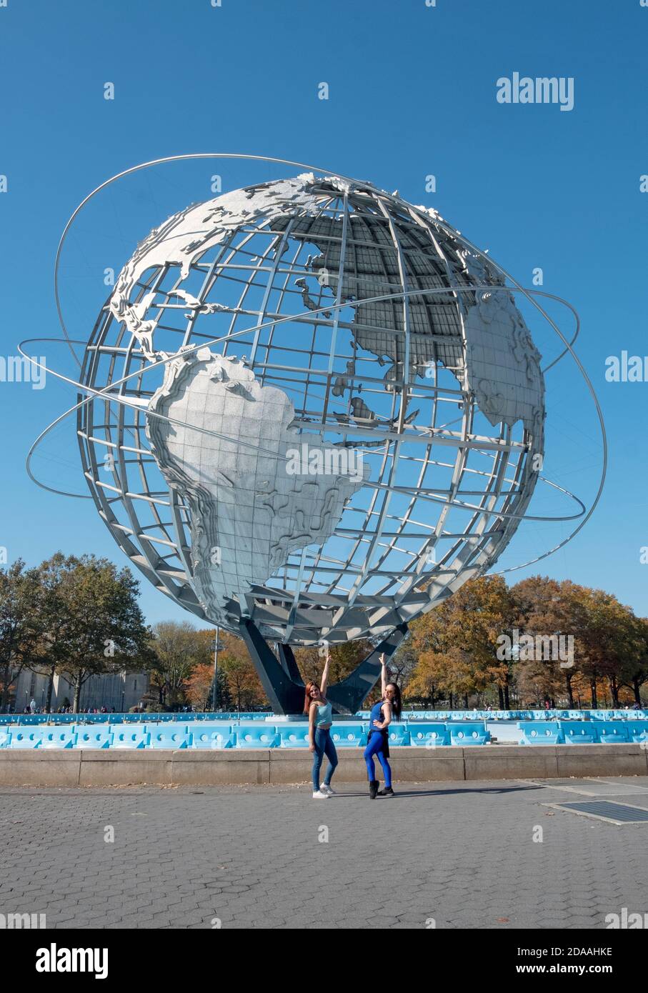 An einem milden Herbsttag posieren 2 attraktive junge Damen vor der Unisphere im Flushing Meadows Corona Park in Queens, New York City Stockfoto