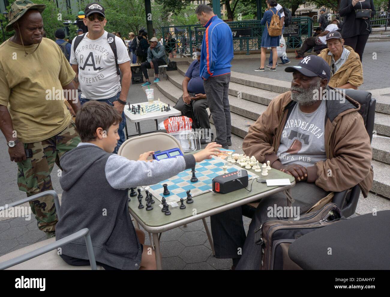 Ein Teenager spielt Schach gegen einen älteren Mann, während mehrere Menschen auf. Im Union Square Park in Lower manhattan, New York City. Stockfoto