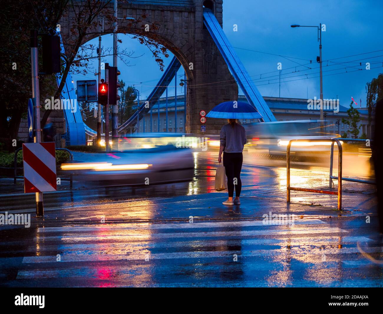 Frau mit Regenschirm an einem regnerischen Abend auf dem Fußgängerüberweg Stockfoto