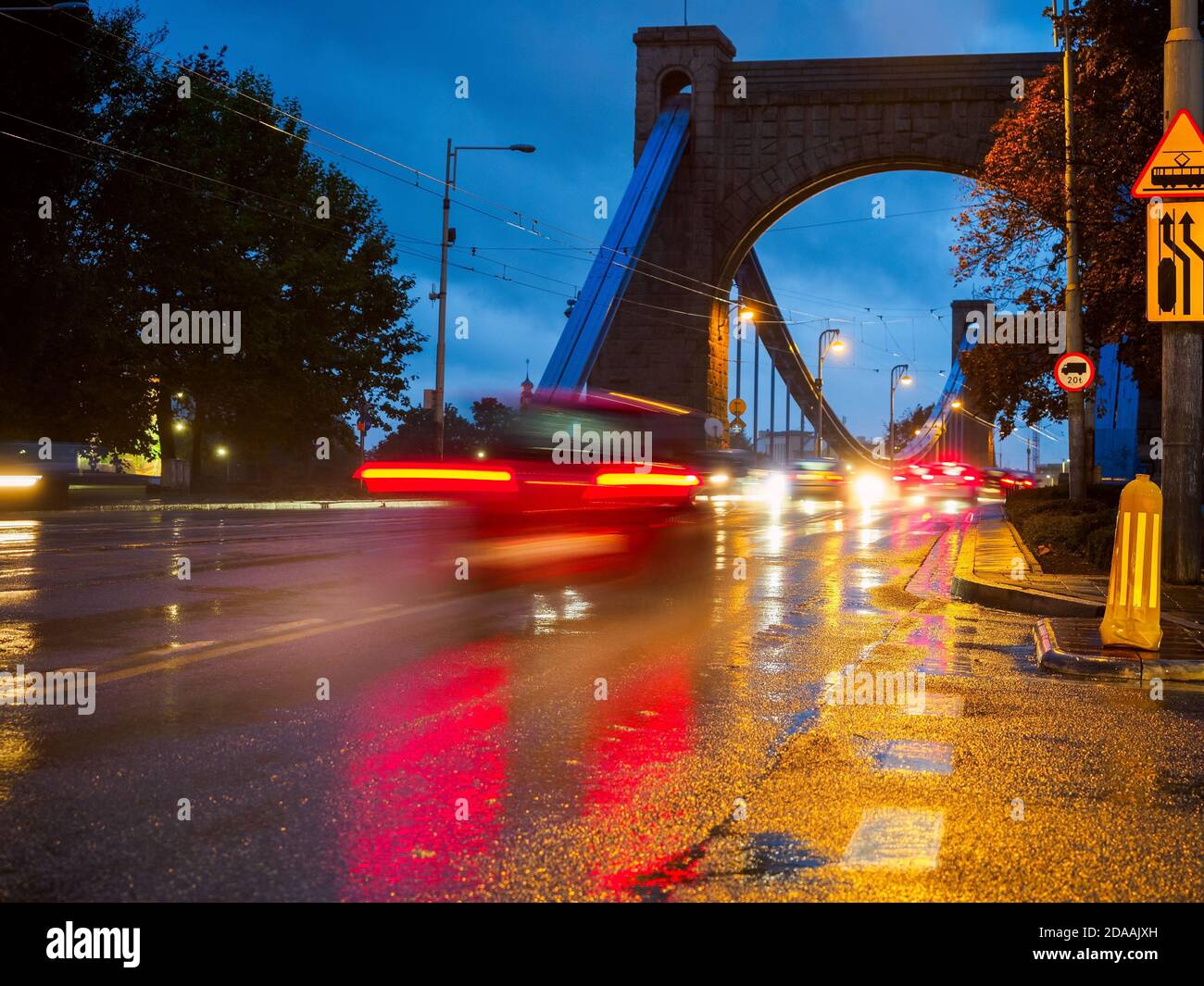 Regnerische Stadtstraße in der Nacht, nächtlicher Verkehr auf nasser Straße bei Regen, Straßenbeleuchtung in Pfützen reflektiert. Stockfoto