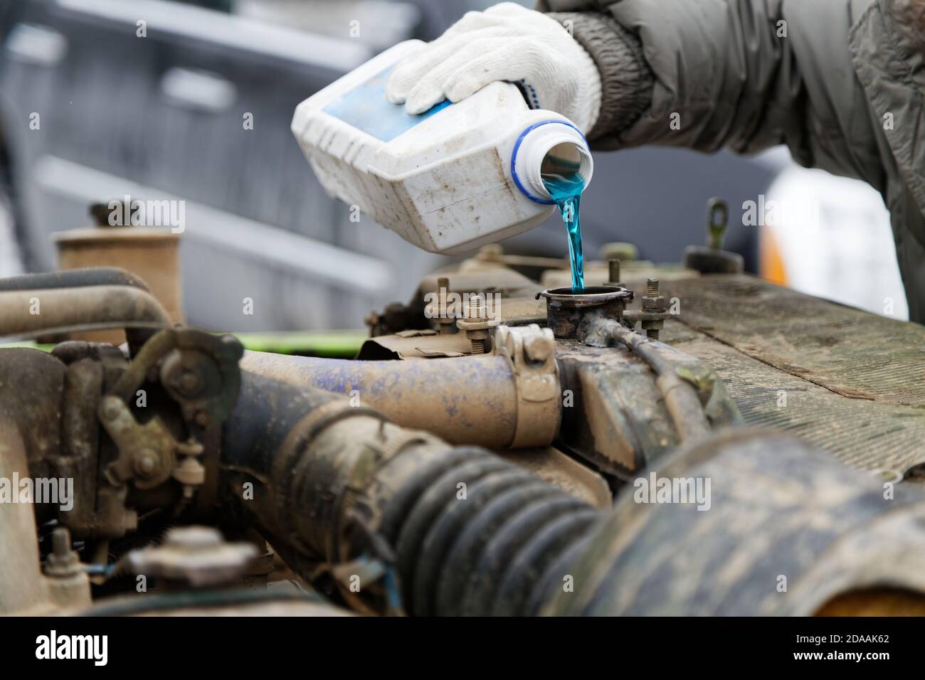 Ein Automechaniker gießt Frostschutzmittel in den Kühler eines alten Automotors. Geringer Fokus. Stockfoto
