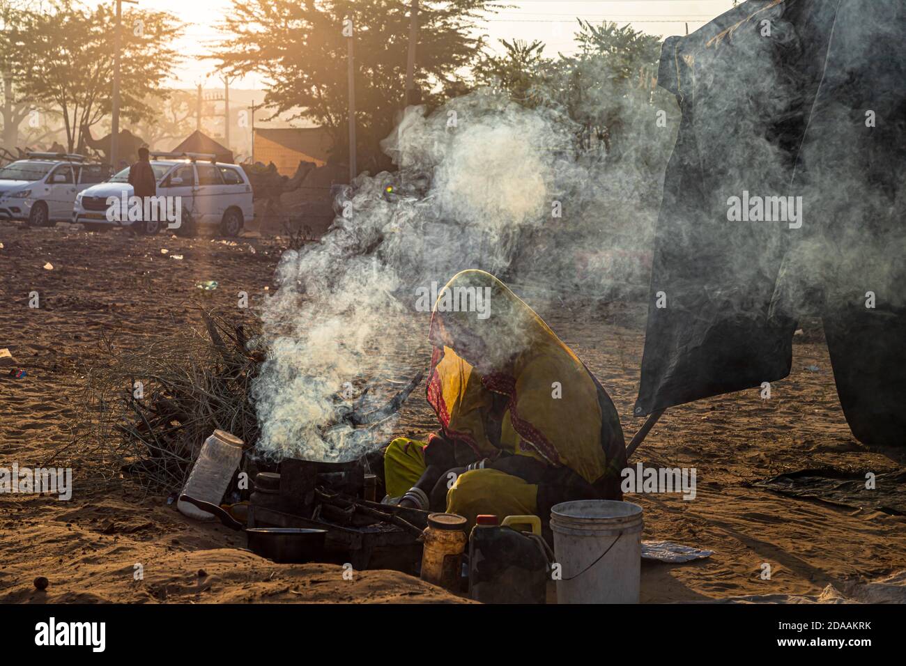 Eine indische Frau, die Essen macht, Rauch kommt aus dem handgefertigten Tonofen im Hintergrund. Stockfoto